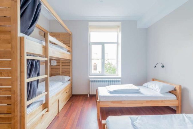 Chambre d'amis fonctionnelle avec lits superposés en bois et lit simple à cadre en bois sur parquet rouge, idéale pour aménager une chambre d'amis pouvant accueillir plusieurs personnes.