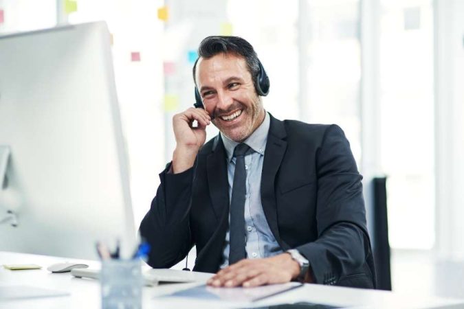 Un conseiller client souriant portant un casque audio travaille sur un ordinateur de bureau dans un centre d'appels moderne.