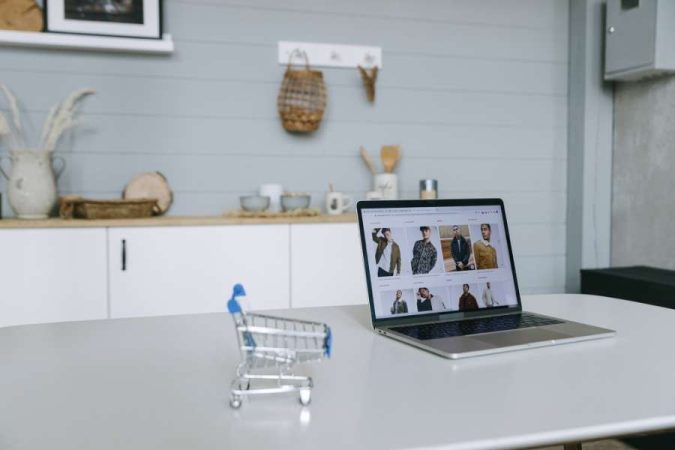 Un ordinateur portable ouvert affiche une boutique de vêtements en ligne à côté d'un mini caddie de courses.