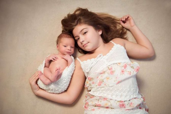 Une grande sœur attentionnée est allongée à côté du nouveau-né pour célébrer l'arrivée d'un petit frère.